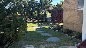 A residential garden with a paved pathway, a wooden fence, and a brick building.
