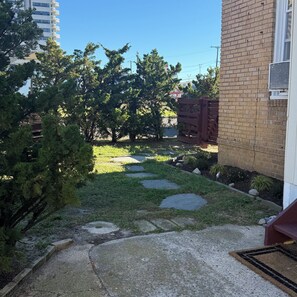 Un jardín residencial con un sendero pavimentado, una cerca de madera y un edificio de ladrillo.