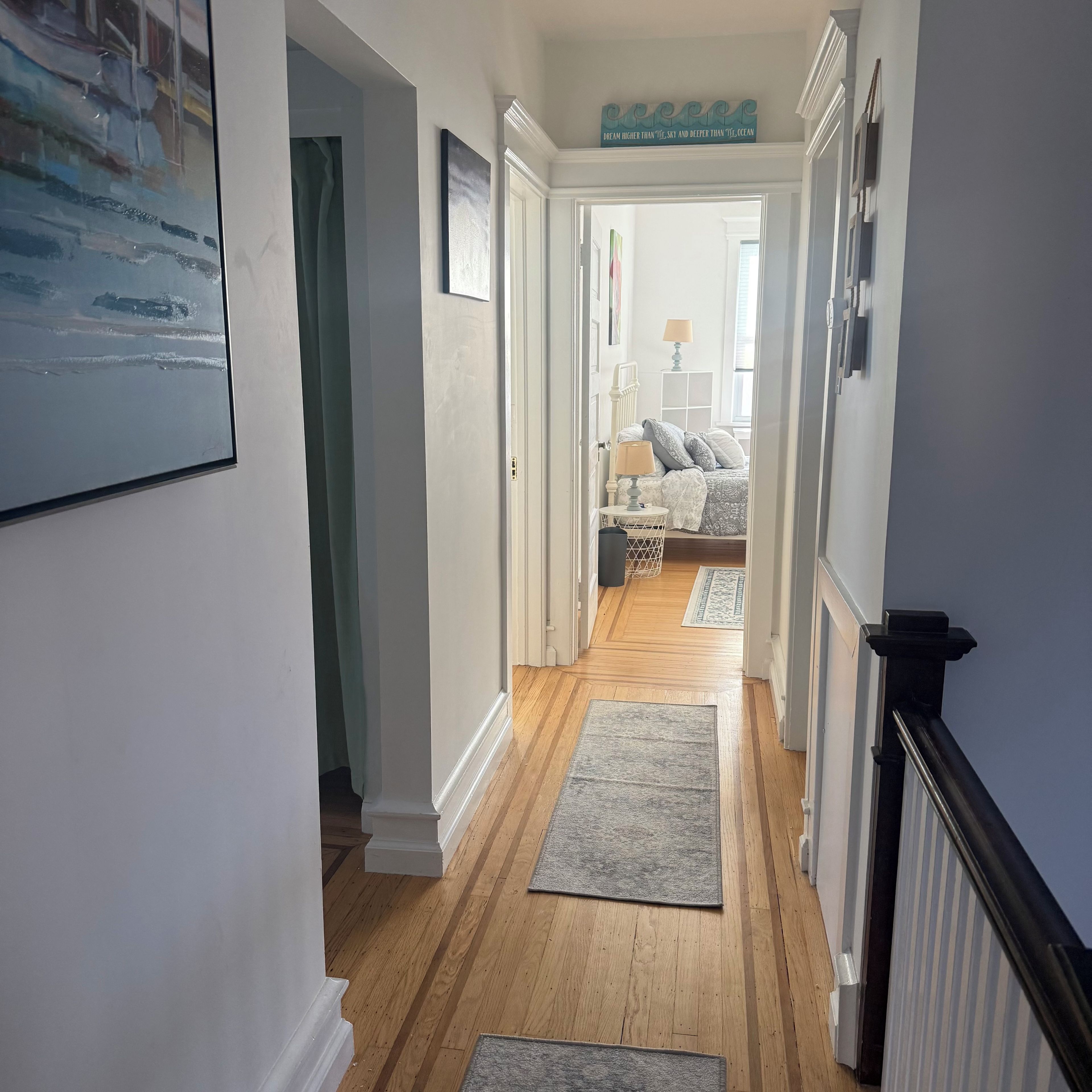 A hallway with wooden flooring, a bed with a patterned bedspread, and a decorative sign above the bed.