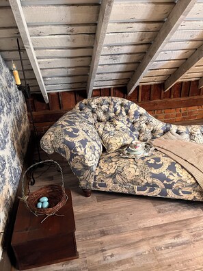 Un cuarto estilo loft con vigas de madera a la vista, un sofá estampado, una cesta de mimbre con huevos y una pared de ladrillo.