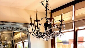 A dining room with a long table, white chairs, a chandelier, and a window with a view of the outside. - Adorable Old World Livery Stable with balcony overlooking Downtown Madison (Madison)