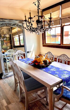 A dining room with a long table, white chairs, a chandelier, and a window with a view of the outside. - Adorable Old World Livery Stable with balcony overlooking Downtown Madison (Madison)