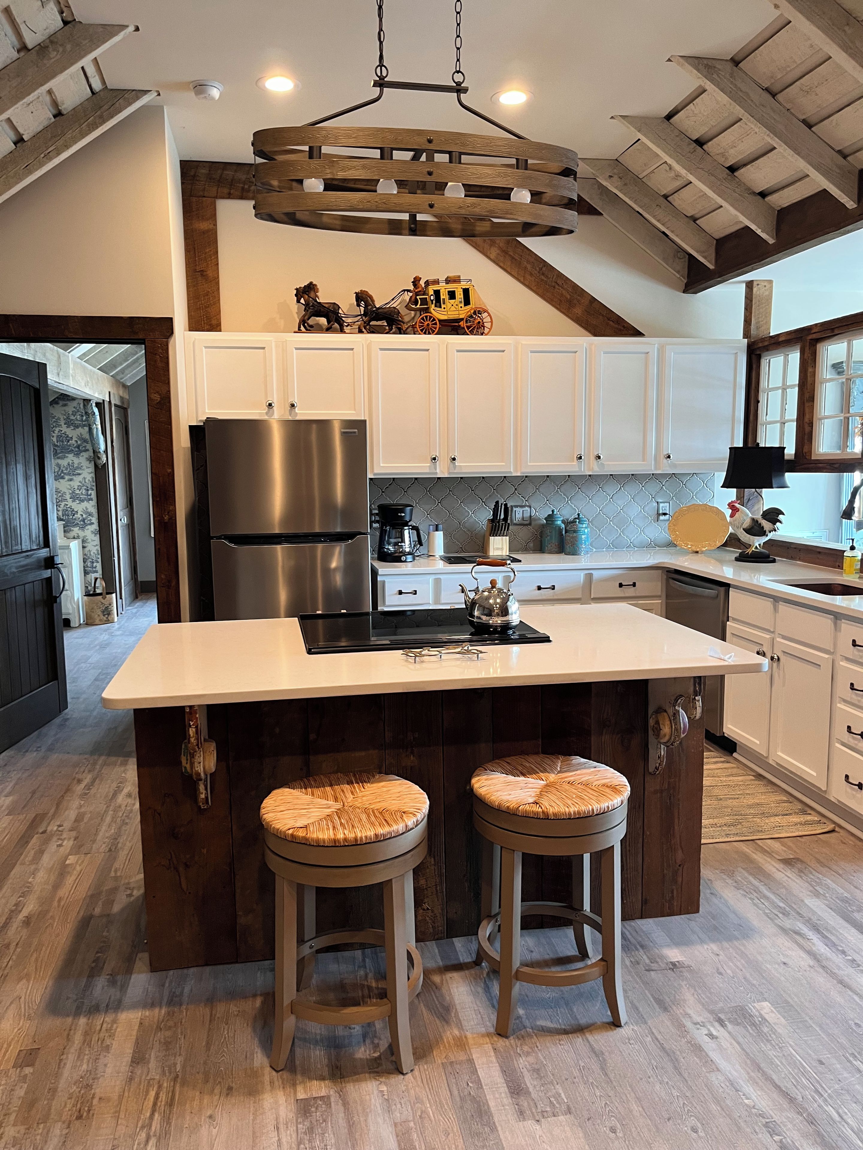 A modern kitchen with a central island, wooden stools, and a decorative horse carriage.