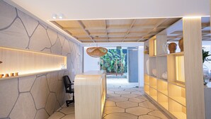 Uma área de recepção com design moderno, destacando um balcão de madeira, uma parede de pedra e um teto com padrão geométrico.