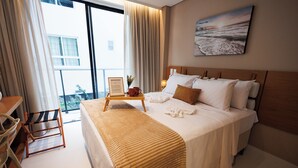 Quarto de hotel com cama, mesa de cabeceira com abajur, uma cadeira e janela com cortinas.