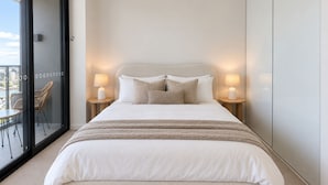 Een slaapkamer met een groot bed, twee bedlampen, uitzicht door een glazen deur en een balkon met rieten meubels.