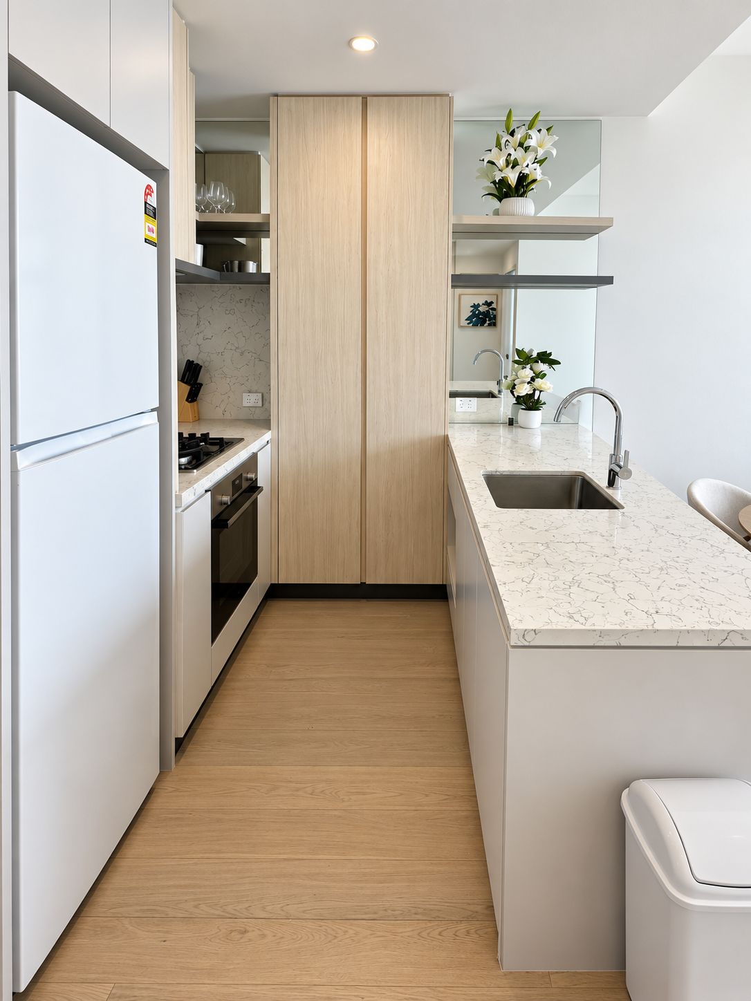 A modern kitchen with white cabinetry, a marble countertop, and a wooden floor.
