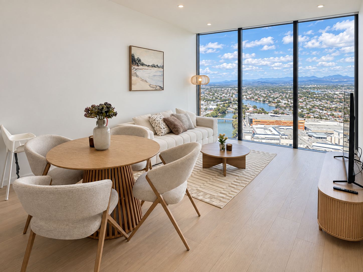 Ein modernes Wohnzimmer mit Essbereich, großen Fenstern und Blick auf die Stadt sowie einem Gemälde an der Wand.