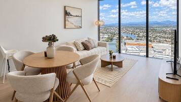Ein modernes Wohnzimmer mit Essbereich, großen Fenstern und Blick auf die Stadt sowie einem Gemälde an der Wand.