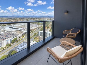 A balcony with wicker chairs and a view of a cityscape, including a large building and mountains in the distance. - The Star Highlife - Views Above Broadbeach (Broadbeach)