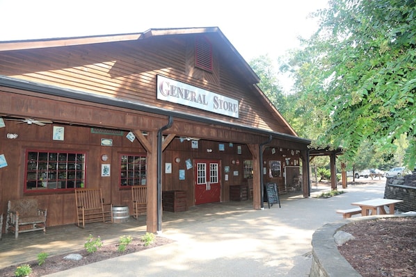 A wooden building labeled 'GENERAL STORE' with a covered entrance, windows, and outdoor seating area.