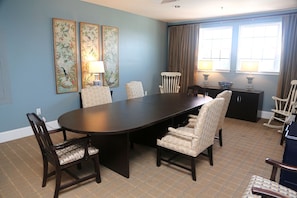 A dining area with a large table, six chairs, two wall-mounted lamps, and a window with curtains.