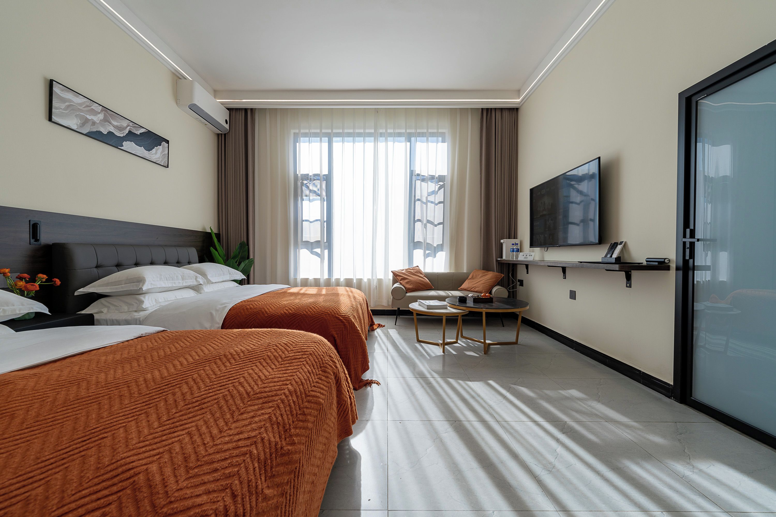 A hotel room with two beds, a sofa, a TV, and a desk.