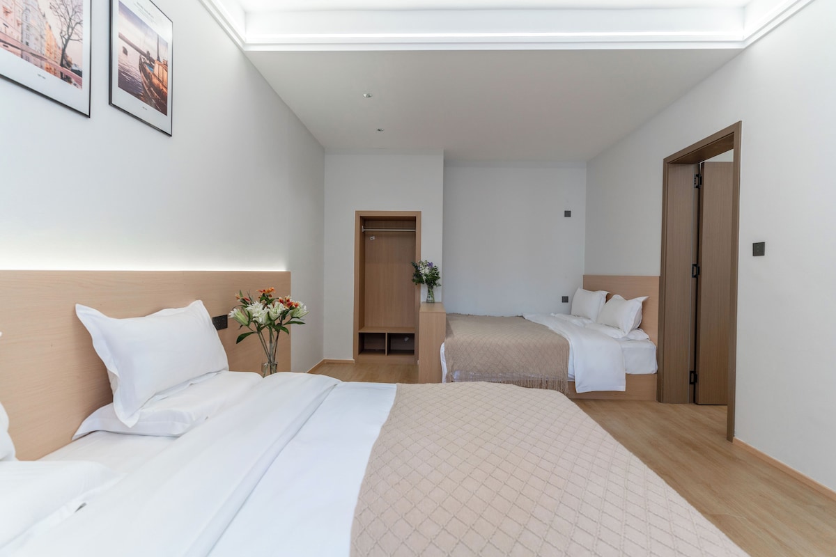 Habitació d'hotel amb dos llits, un panell de fusta al capçal, un escriptori petit i una porta.