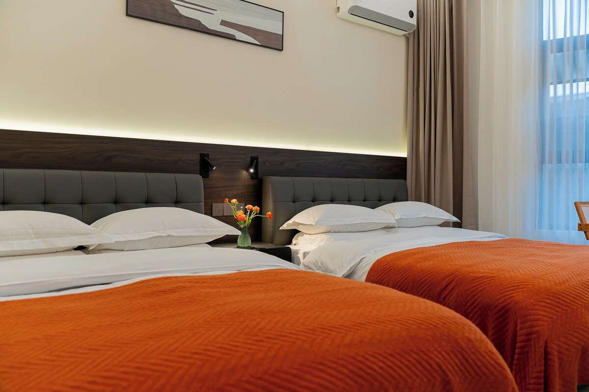 Habitació d'hotel amb dos llits, una tauleta de nit, un vas amb flors i un quadre a la paret.