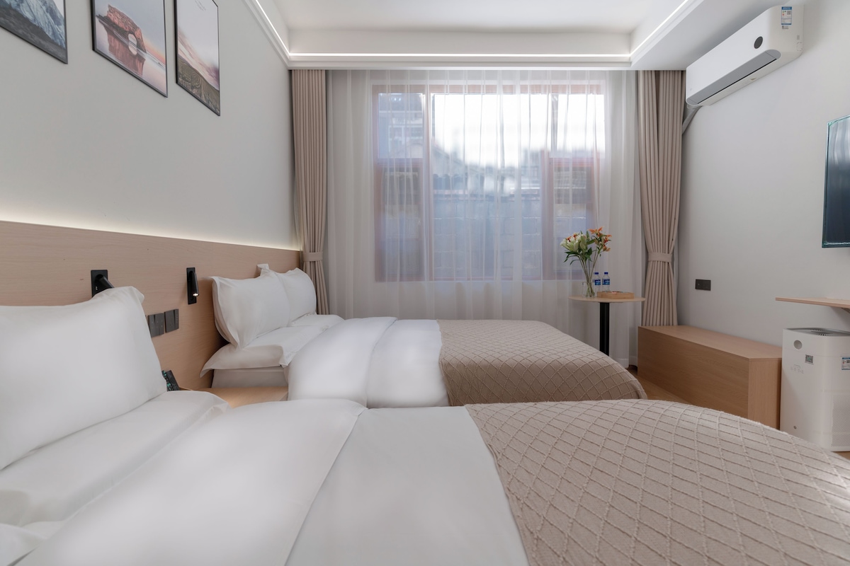 Habitació d'hotel amb dos llits, una taula petita amb un ram de flors i un televisió de pantalla plana penjada a la paret.