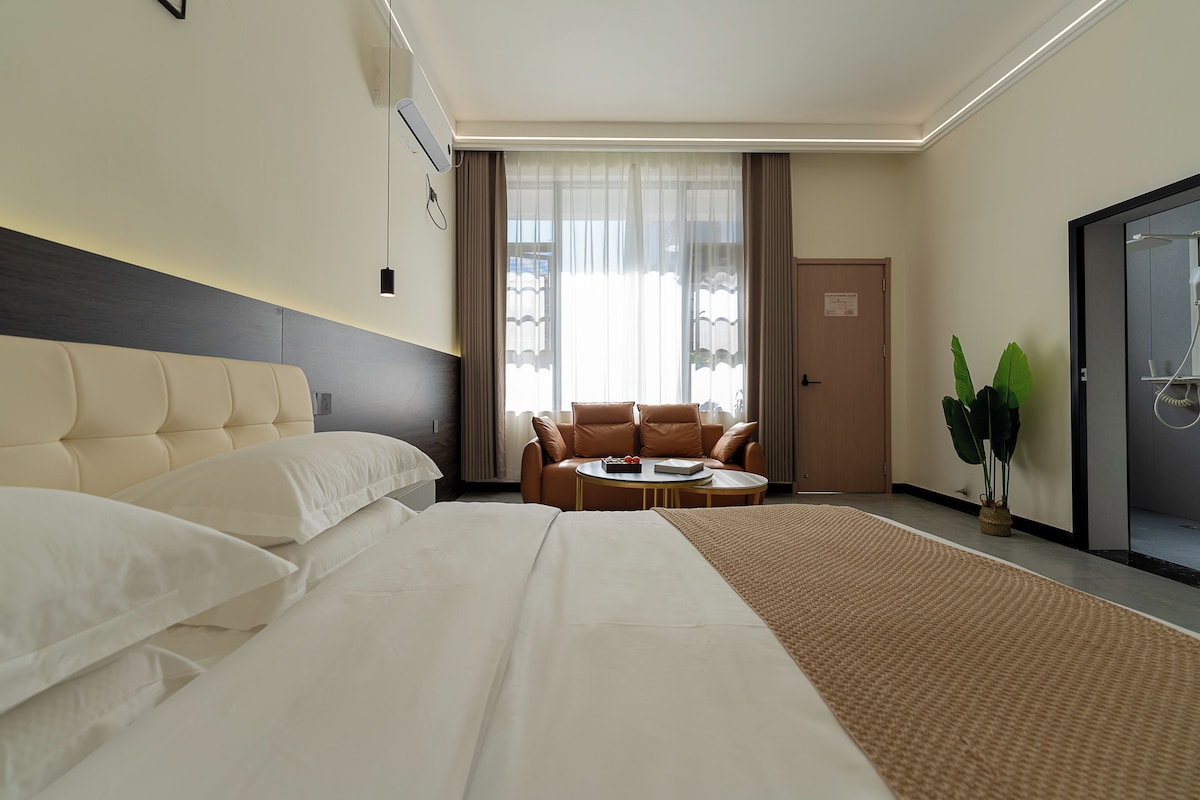 Habitació d'hotel amb un llit gran, un sofà, una taula petita i una planta en test.