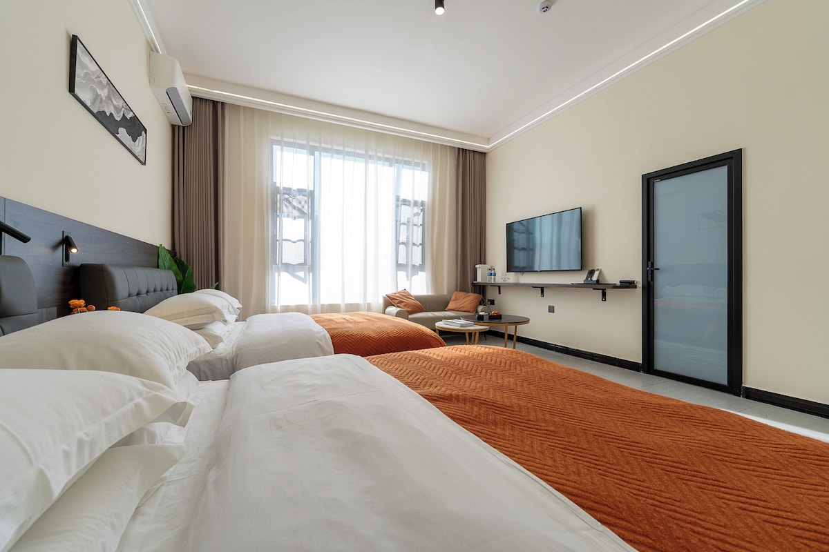 Habitació d'hotel amb dos llits, un sofà, una televisió i una porta corredissa.