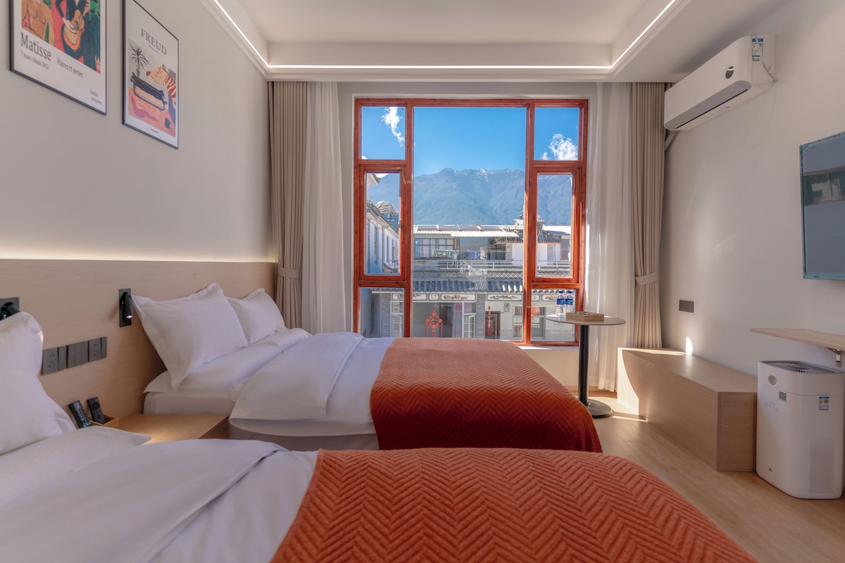 Habitació d'hotel amb una finestra gran, un llit, una taula de treball i una cadira.