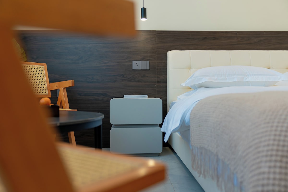 Una habitació d'hotel ben ordenada amb un llit, una taula de nit, una cadira i una taula petita amb una làmpada.
