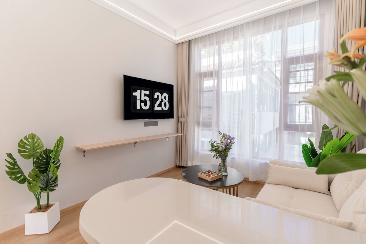 Un saló modern amb televisió plana que mostra l'hora, un sofà, una taula de centre i una planta en test.