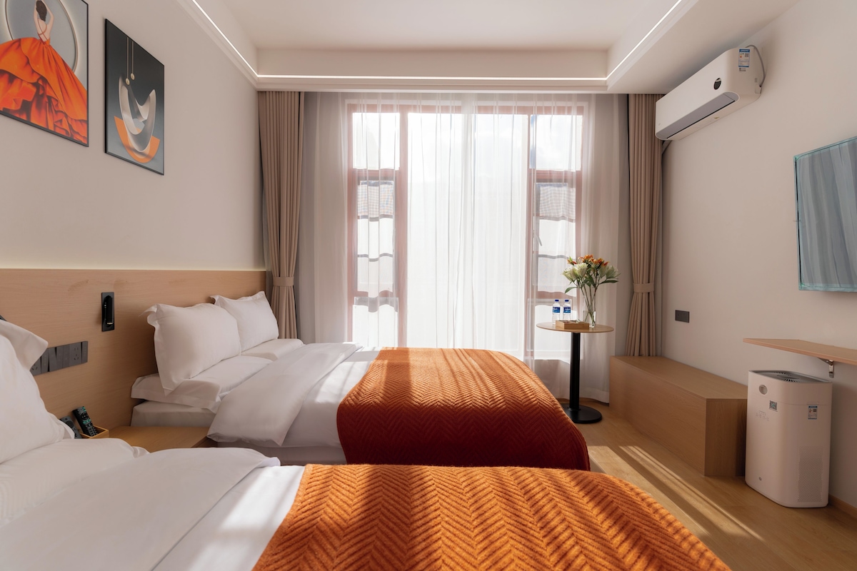 Habitació d'hotel amb dos llits, una taula petita amb un ram de flors, un aparell d'aire acondicionat i una prestatgeria penjada a la paret.