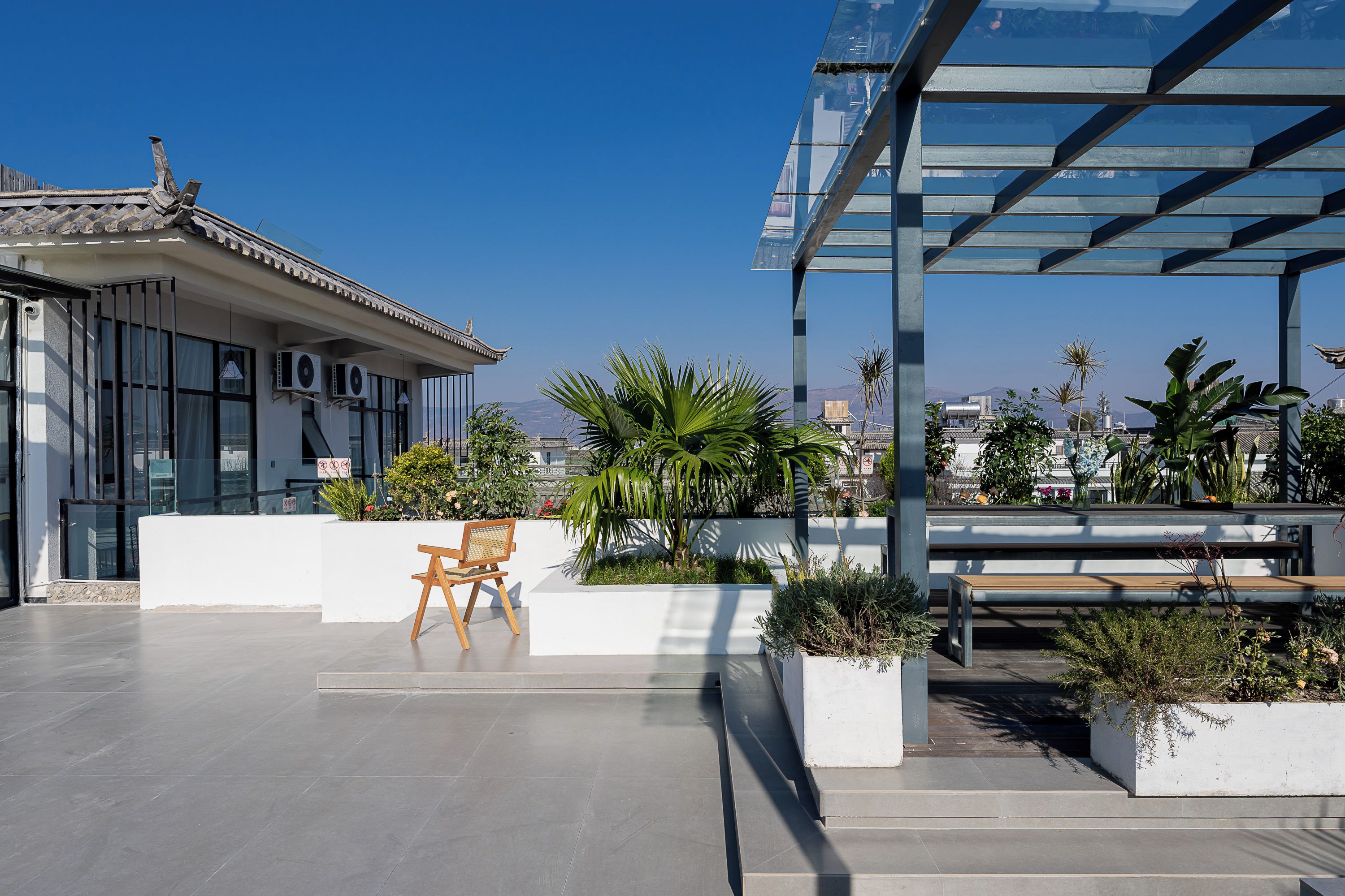 A rooftop terrace with a traditional building, modern seating, and potted plants.