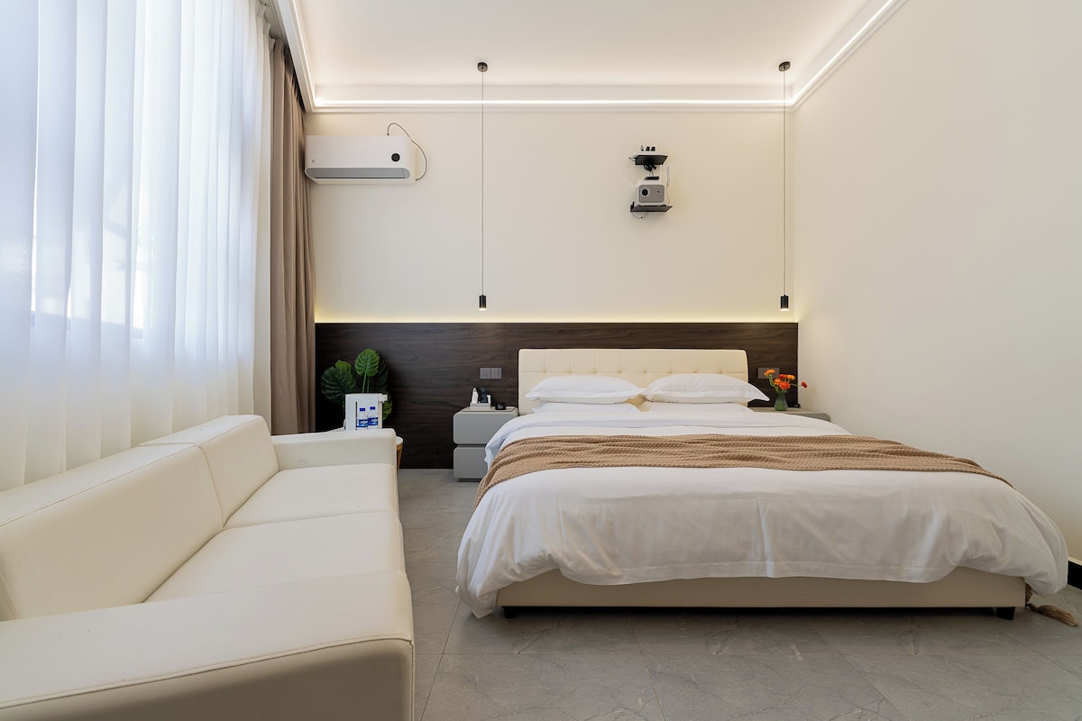 Habitació d'hotel moderna amb llit, sofà, tauleta de nit i aire condicionat fixat a la paret.