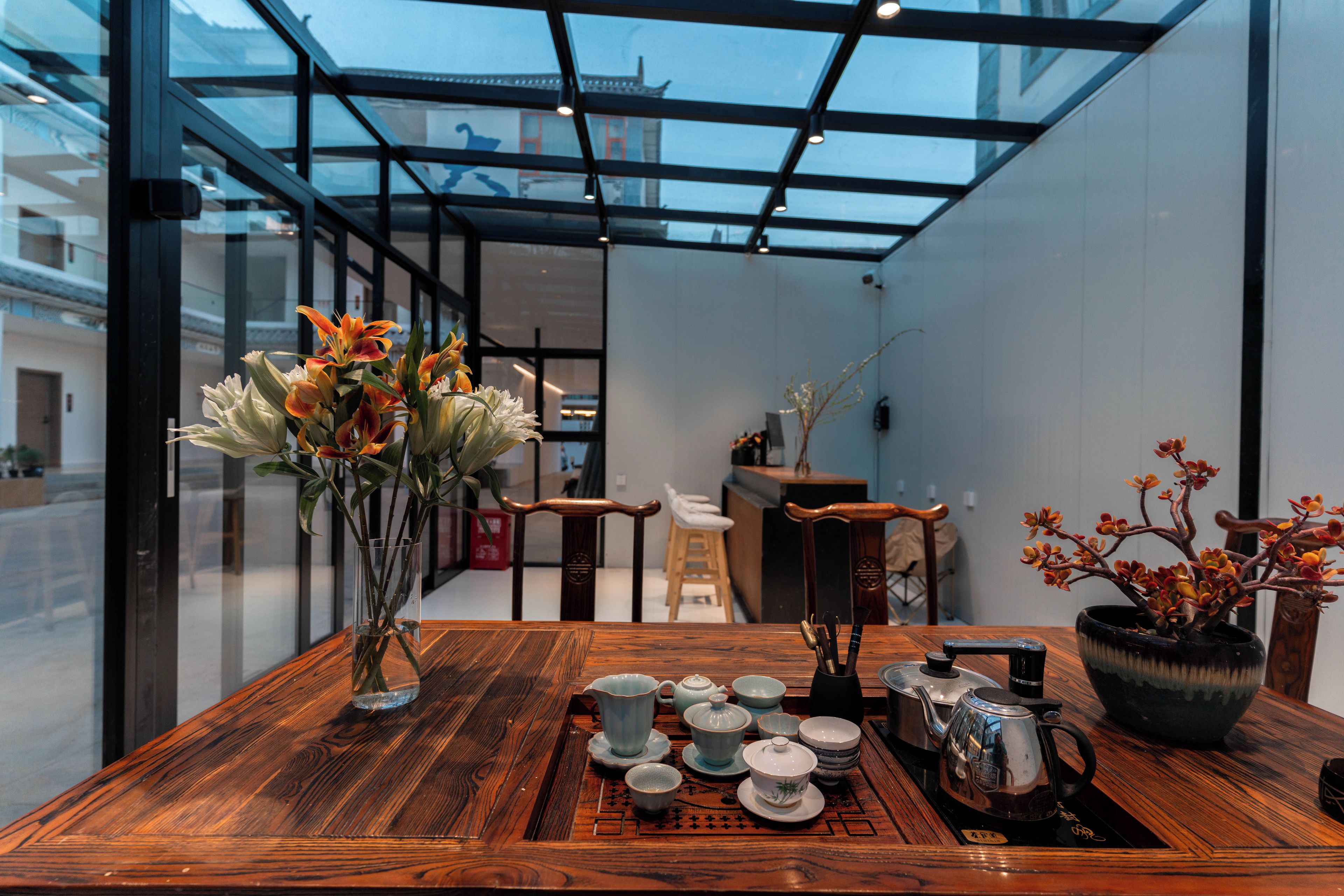Una mesa de madera con vajillas de té y un jarrón de flores en un interior moderno con paredes de vidrio.