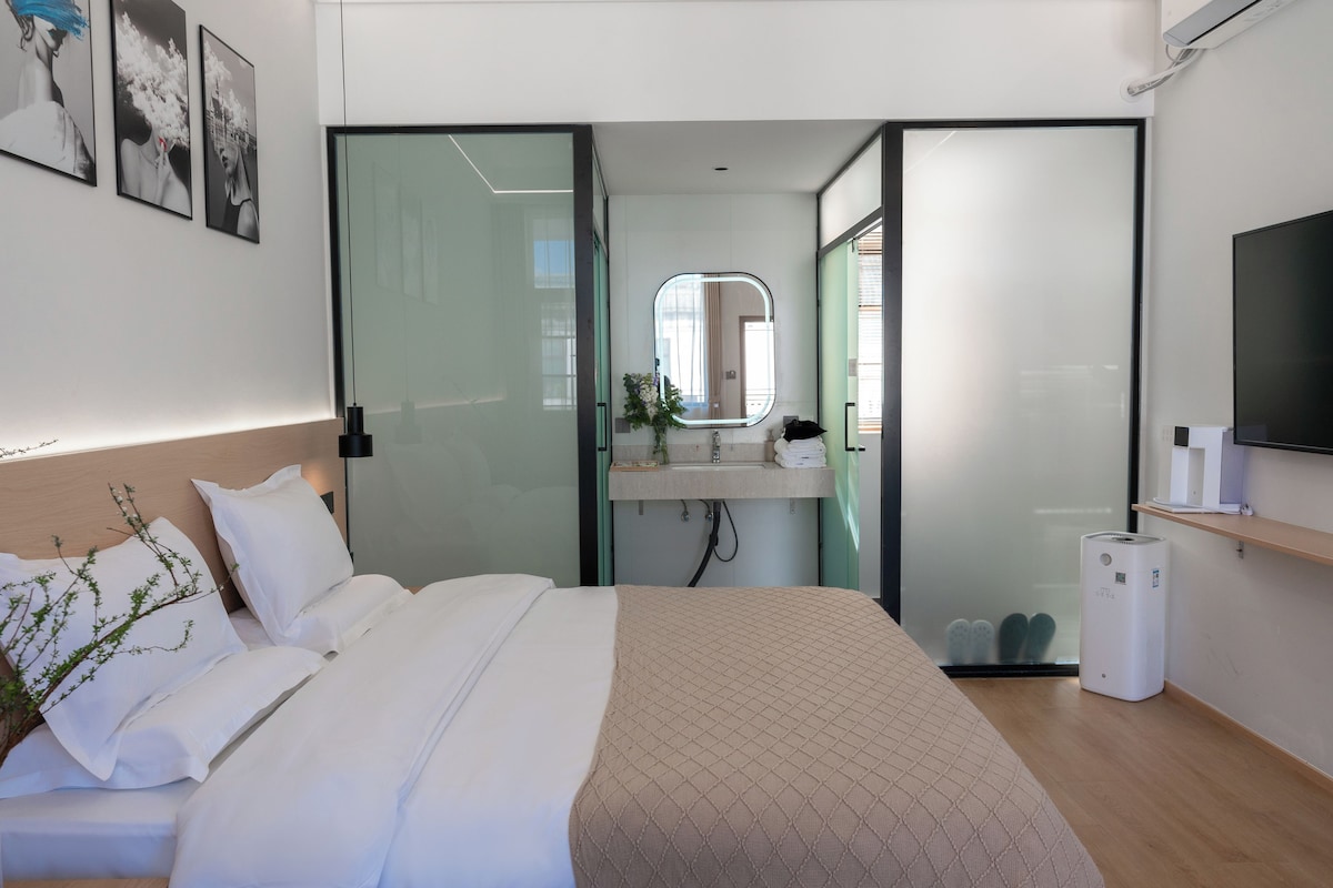 Habitació d'hotel moderna amb un llit, una taula de nit, un mirall, un televisor i una petita planta.