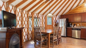A wooden interior with a dining table, chairs, a television, and a kitchen area.