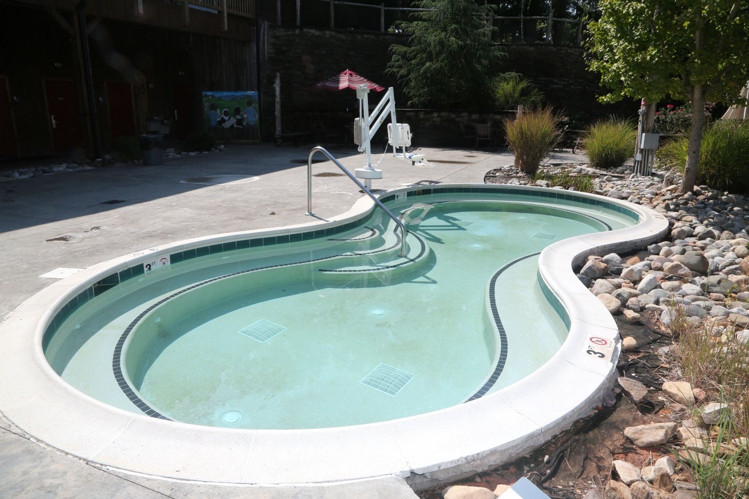 A swimming pool with a curved design, a diving board, and a small covered seating area.