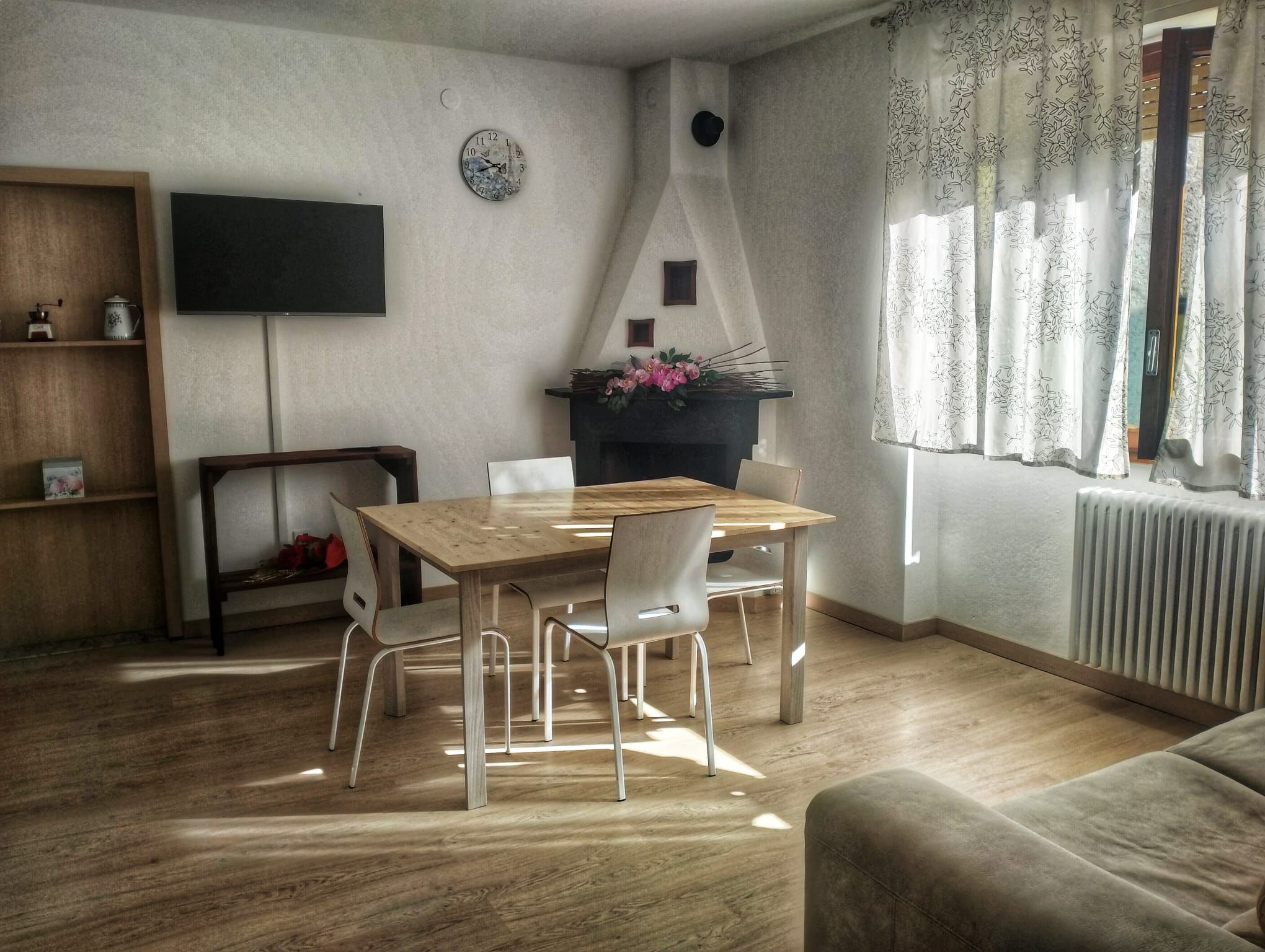 A dining area with a wooden table and chairs, a flat-screen TV mounted on the wall, and a fireplace with a decorative flower arrangement.