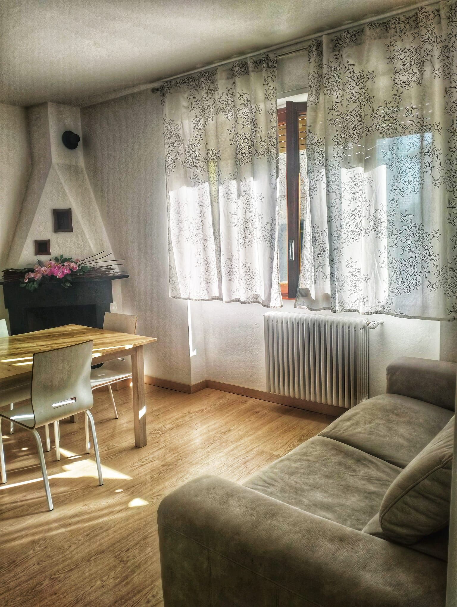 A living room with a sofa, a dining table with chairs, a fireplace, and a window with patterned curtains.