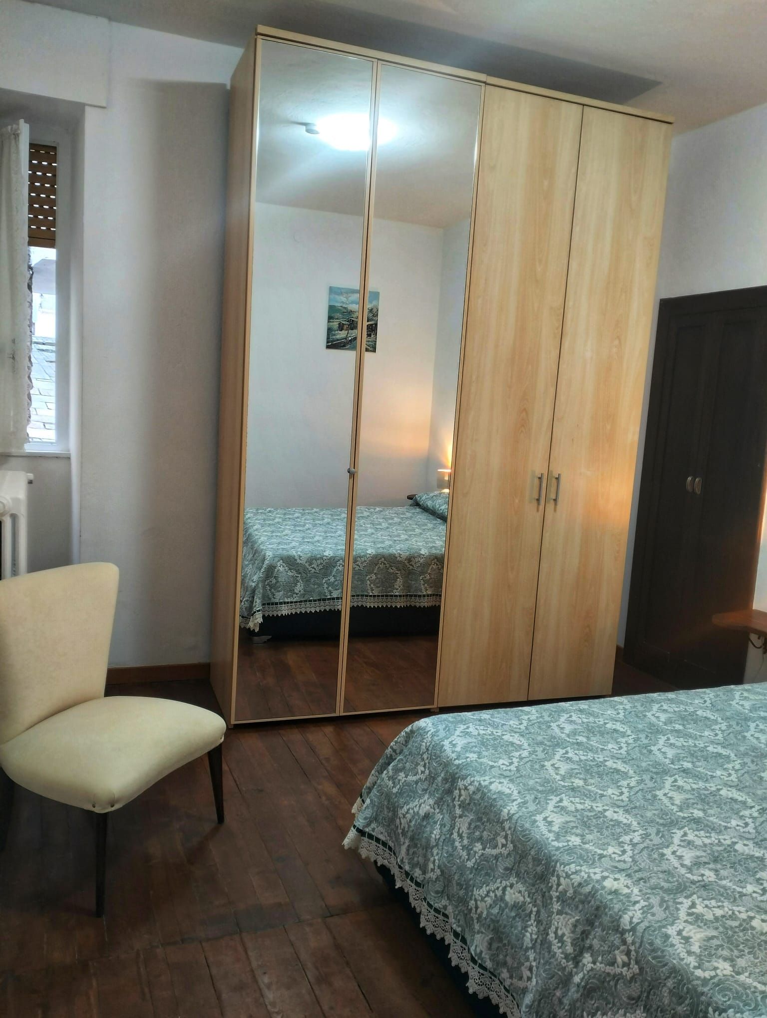 A bedroom with a wardrobe, a chair, and a bed.