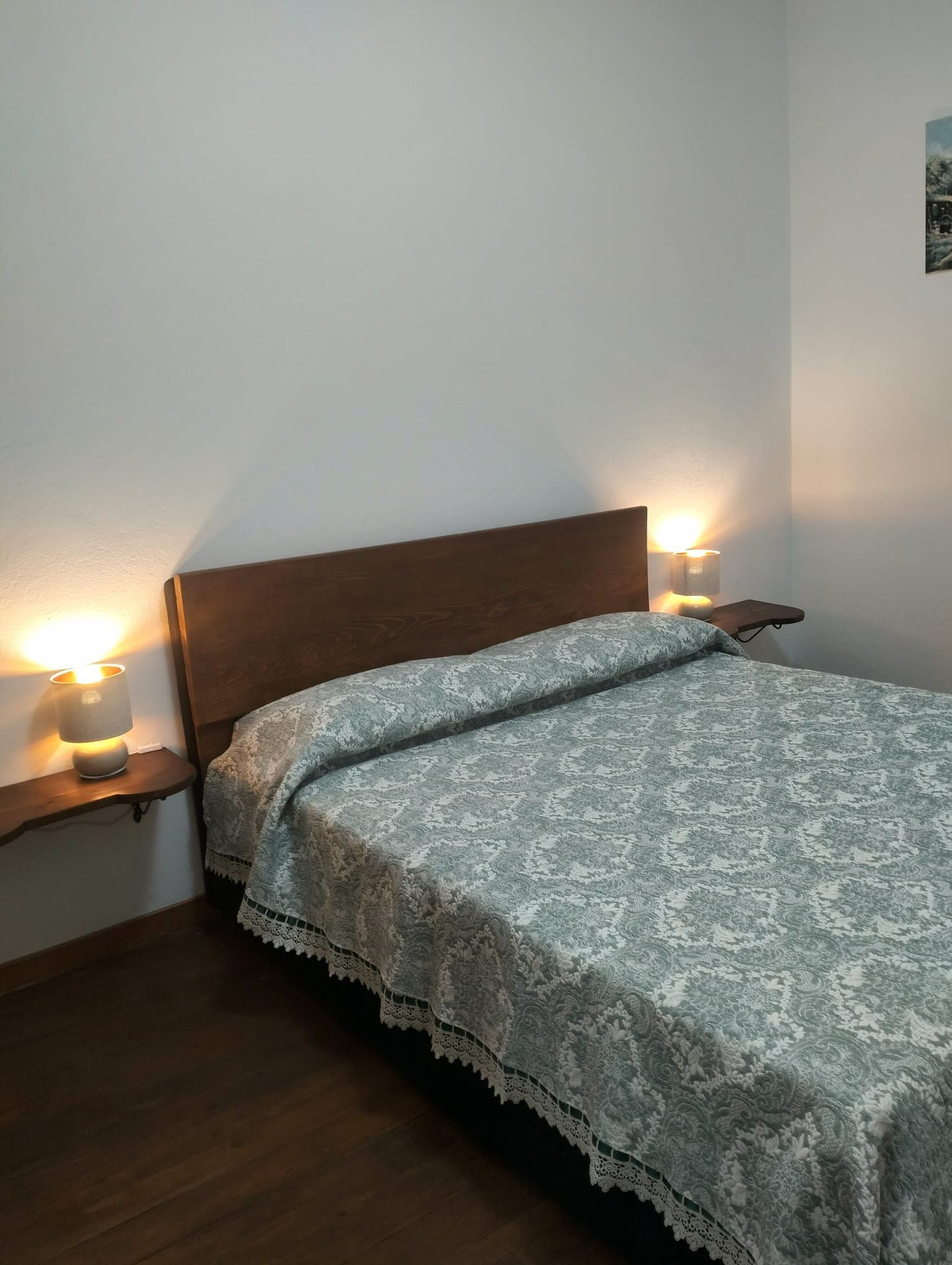 A single bed with a wooden headboard, flanked by bedside tables with lamps, in a room with plain walls and a wooden floor.