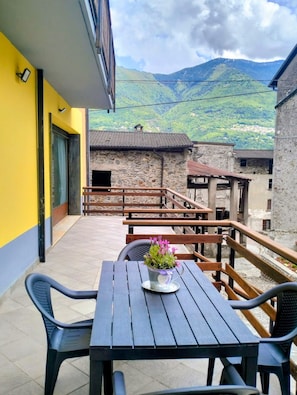 Une terrasse extérieure avec une table et des chaises en bois, un vase de fleurs et une vue sur un paysage montagneux.