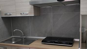 Una cuina moderna amb un vàter d'acer inoxidable, una placa d'inducció negra i armaris de fusta.
