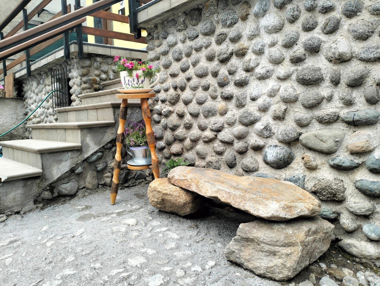 Un mur de pedra amb un relleu, un tamboret de fusta amb una planta en test i una llau d'aquesta pedra.