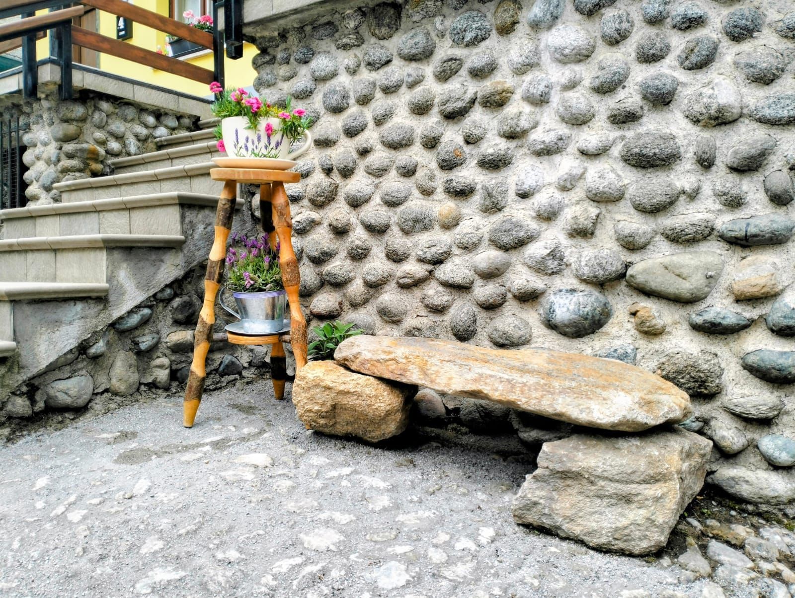 Un muro in pietra con uno sgabello di legno e piante in vaso.