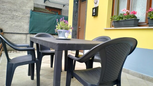 En udendørs terrasse med et bord og stole, en potteplante og en bygning med et nummer på.