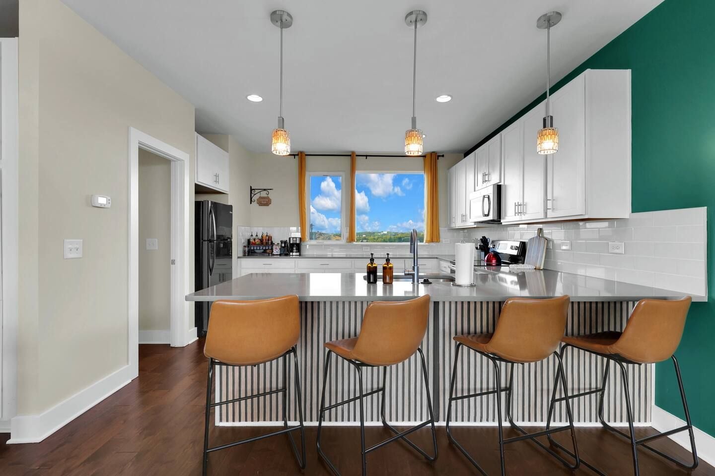 Una cocina moderna con una isla central, taburetes de bar, iluminación colgante y vistas al exterior.