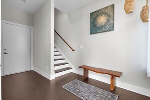A staircase with a wooden handrail, a bench, and a patterned rug in a hallway with white walls and a wooden floor. - Nashville Overlook (Nashville)