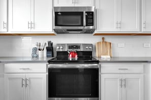 A modern kitchen with white cabinets, a stainless steel microwave, a gas stove, and a wooden cutting board. - Nashville Overlook (Nashville)