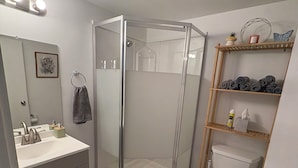 Een badkamer met een douchecabine, een toilet, een wastafel met spiegel en een plank met handdoeken.