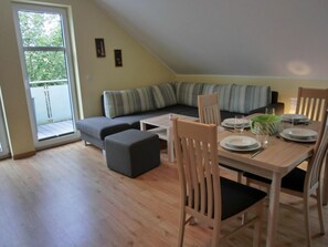 Ein Essbereich mit einem Tisch für vier Personen, einer Couch und einem Fenster mit Blick auf Grünflächen.