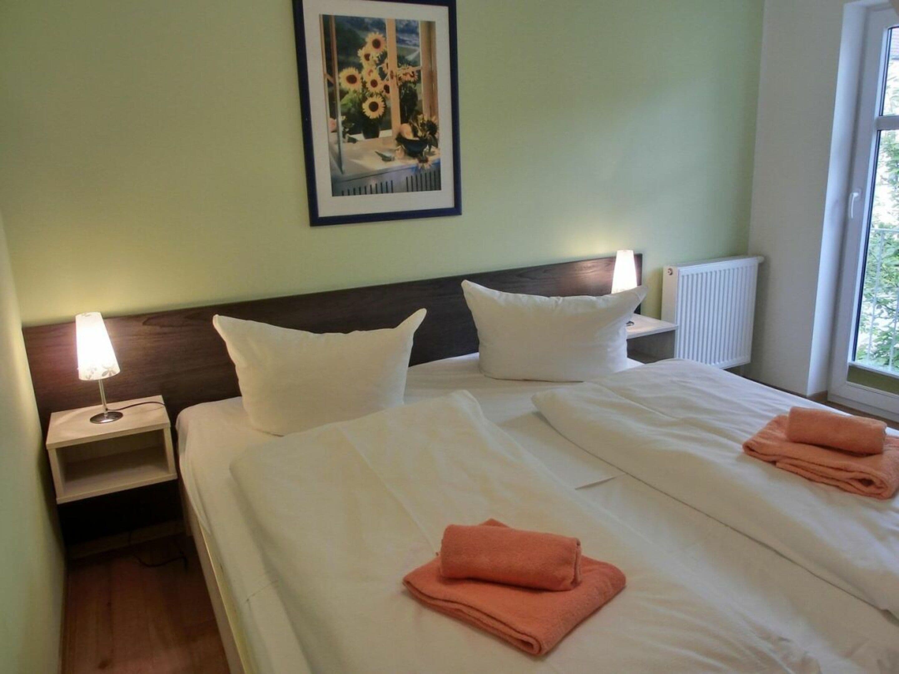 Une chambre d’hôtel avec un lit, deux oreillers, une table de chevet avec une lampe et un tableau encadré au mur.