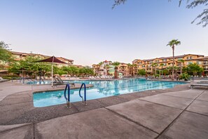 A swimming pool with lounge chairs and a water slide, surrounded by hotel buildings.