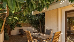Un patio al aire libre con una mesa y sillas, rodeado de follaje y una pared blanca.
