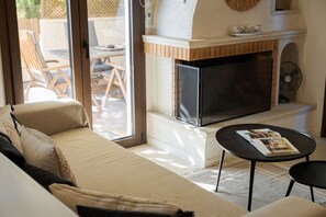 A living room with a sofa, a fireplace, and a table with a magazine. - Casa Smaragdi Aegina (Perdika)